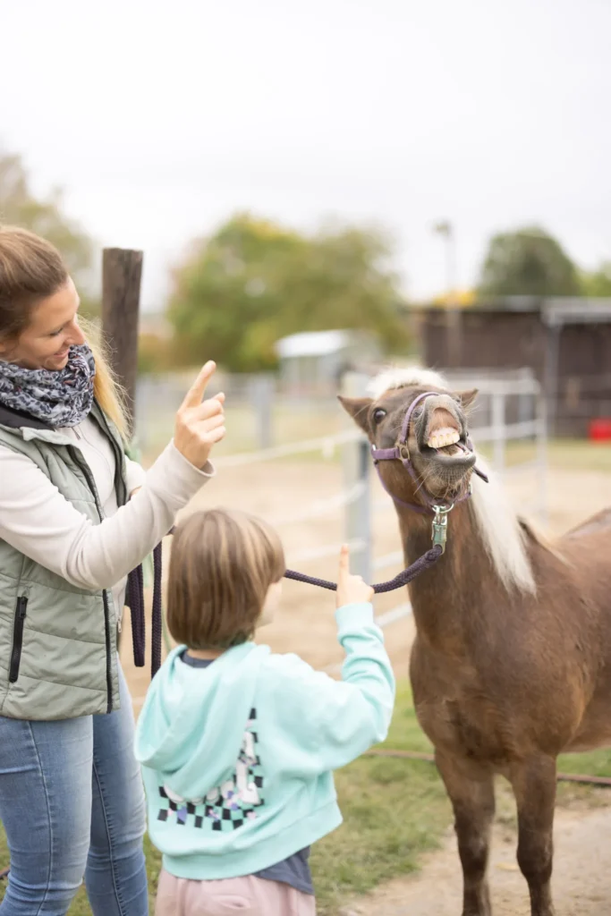 Ein Kind und die Therapeutin stehen bei einem Pony, das die Oberlippe hebt